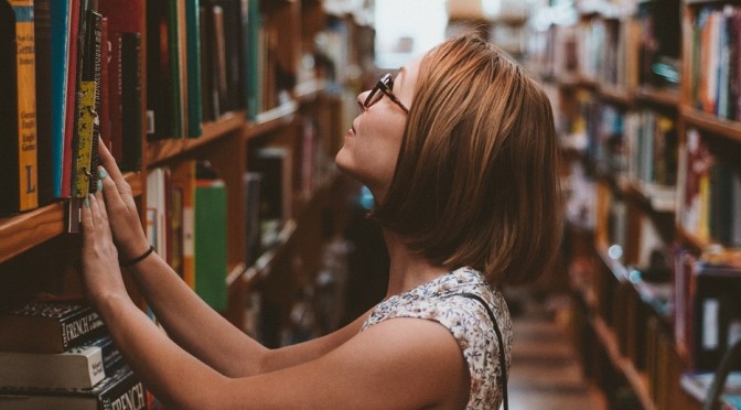 Woman in a library, searching for books on the shelves